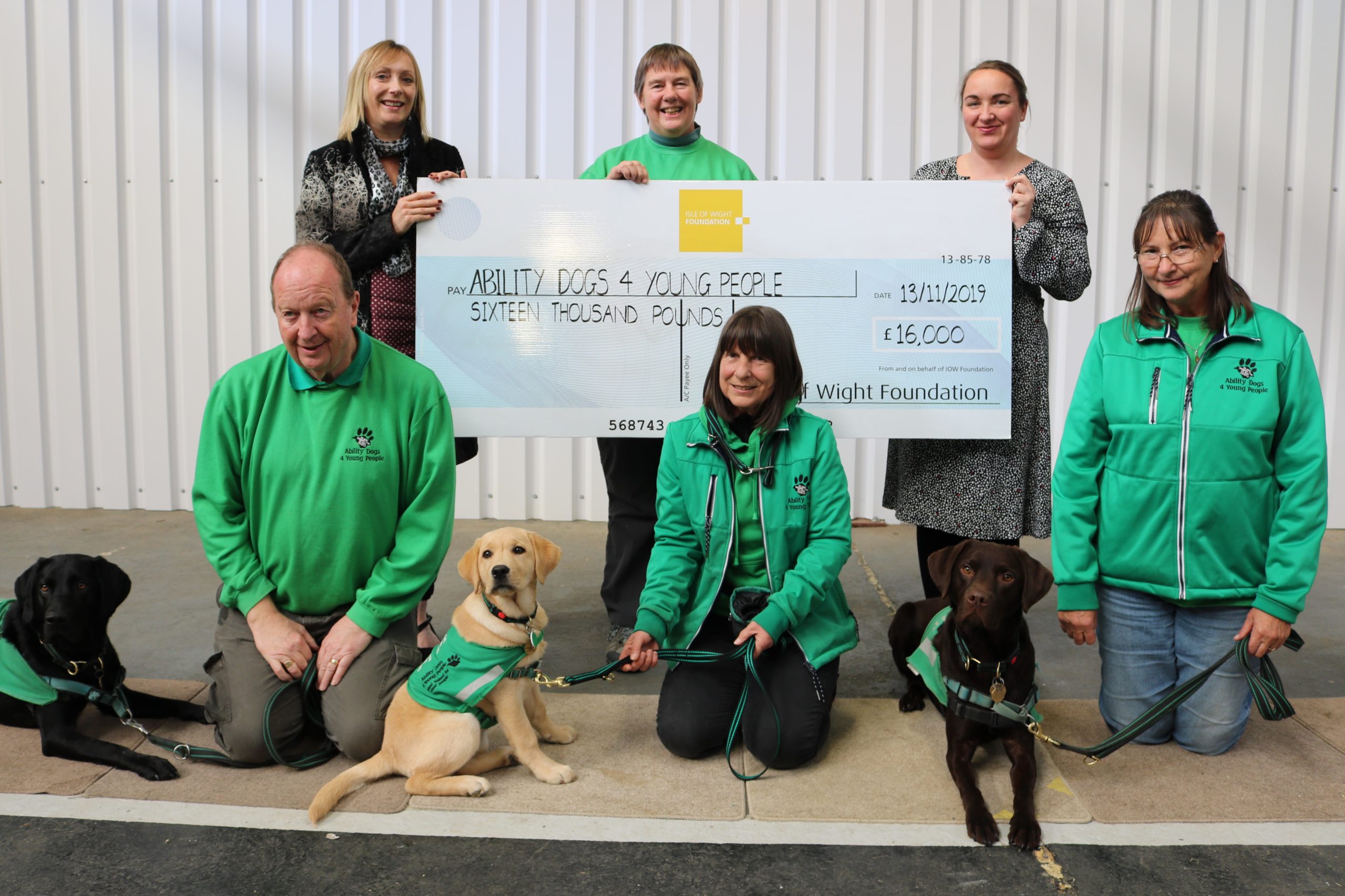 photo showing adults from Island Roads and Ability Dogs for Young People charity with dogs and a large cheque