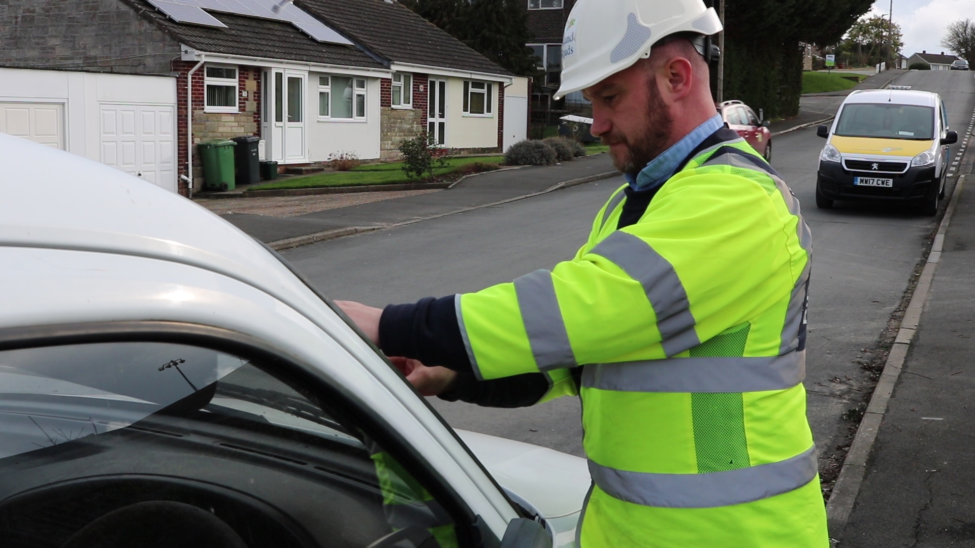 Photo showing Island Roads District Steward affixing a notice to an abandoned vehicle left in the street