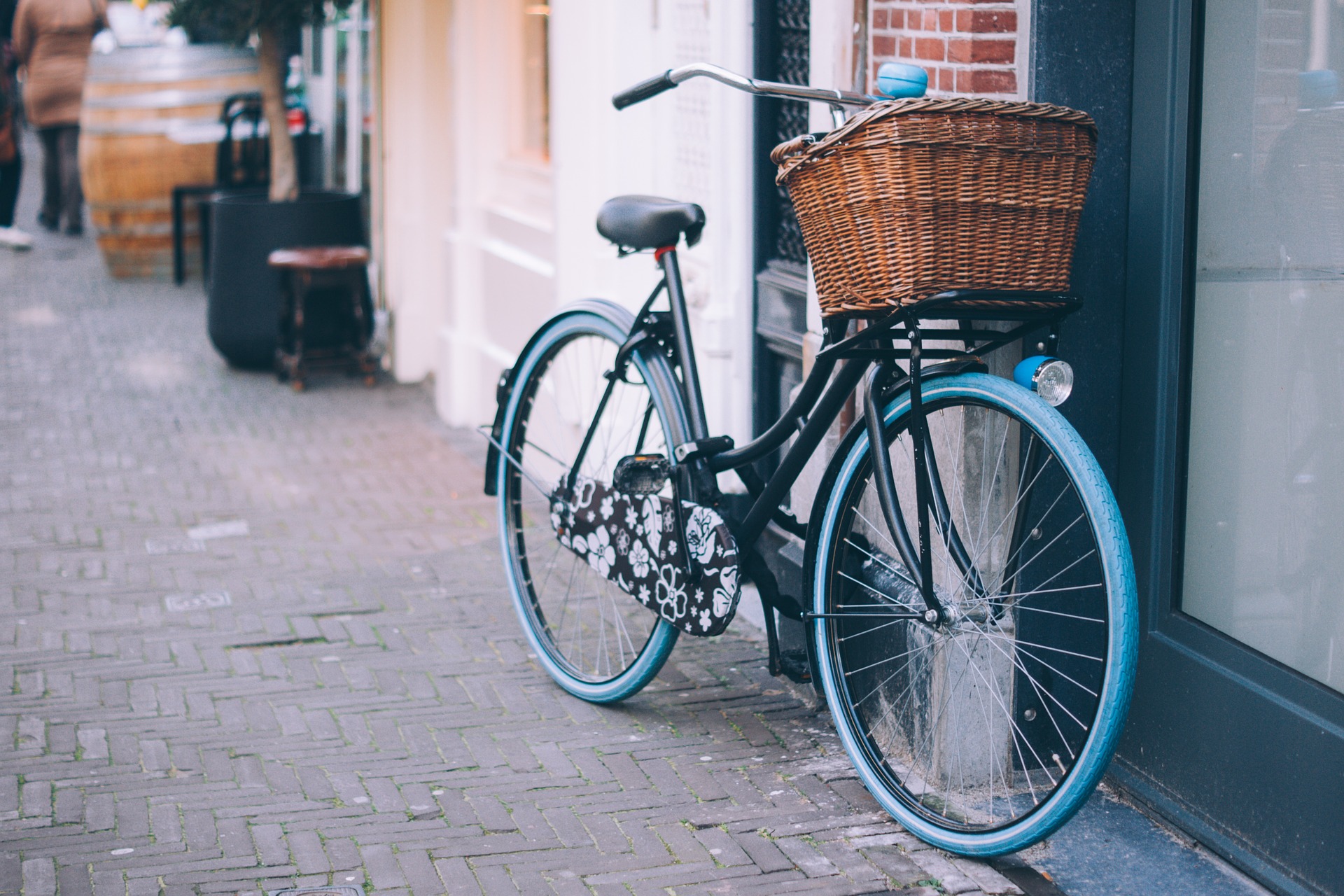 photo showing a bicycle with wicker pannier leaning against a wall in a street, cafe bar in the background