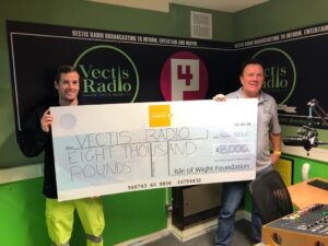 Photo showing two people one from Island Roads and one from Vectis Radio in their studio holding a large cheque