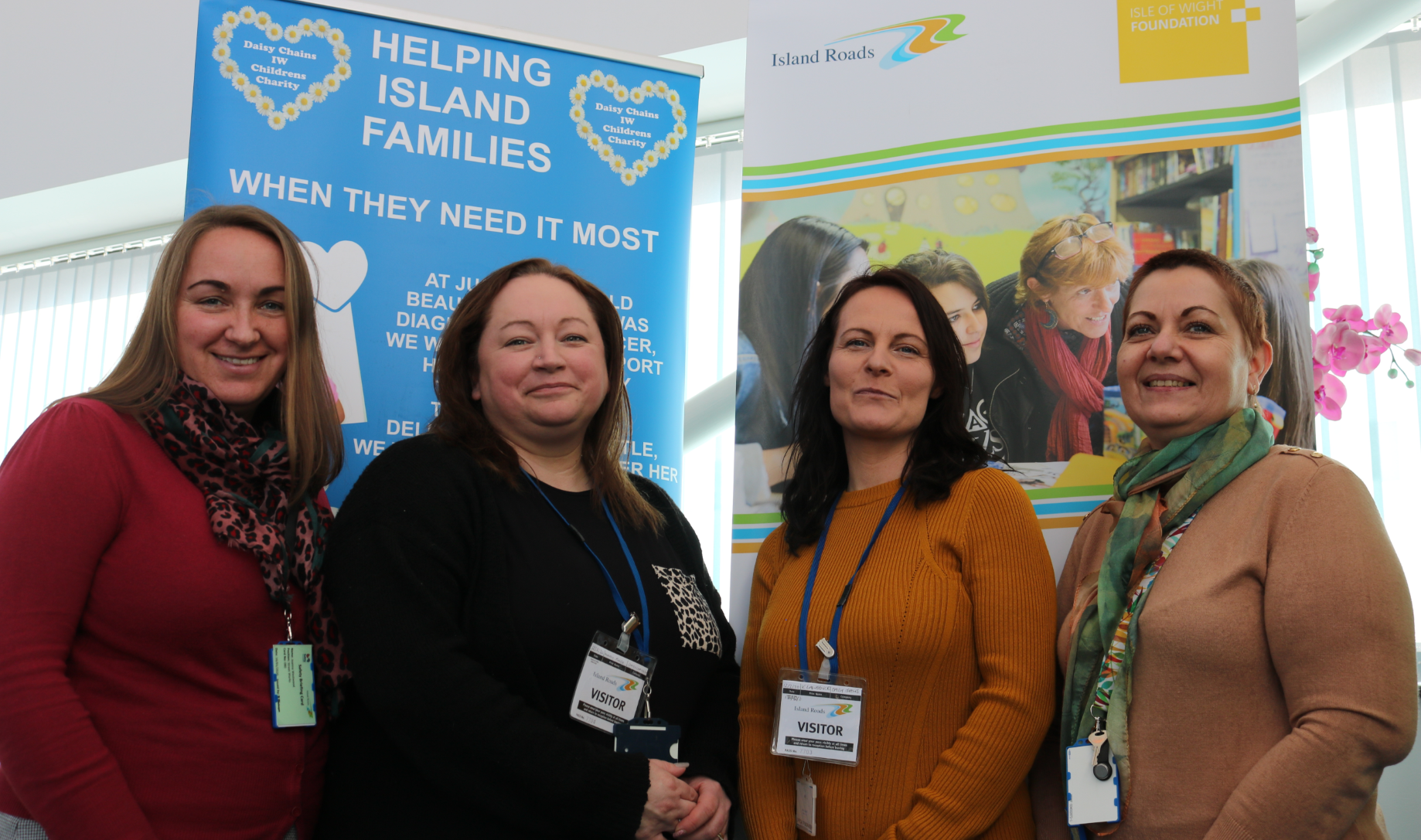 Photo showing four people, two from Daisy Chains charity, two from Island Roads, in front of colourful banners promoting the charity and the IW Foundation