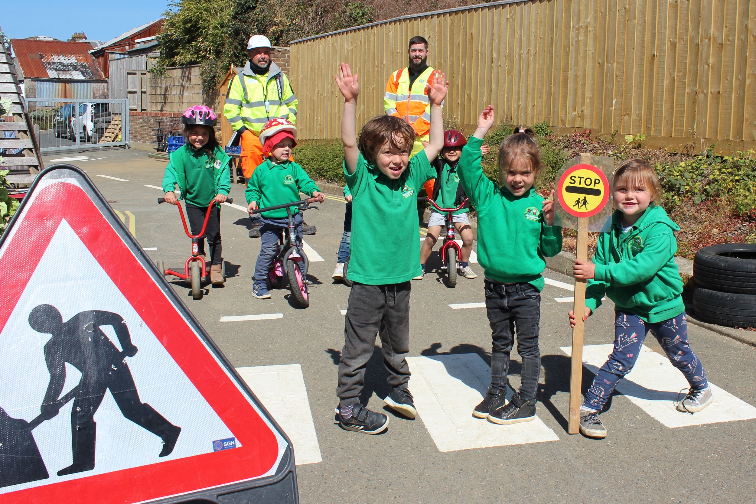 Photo showing school children on a pedestrian crossing that has been marked out on the playground, together with road signs, other children on bikes and Island Roads staff in the background
