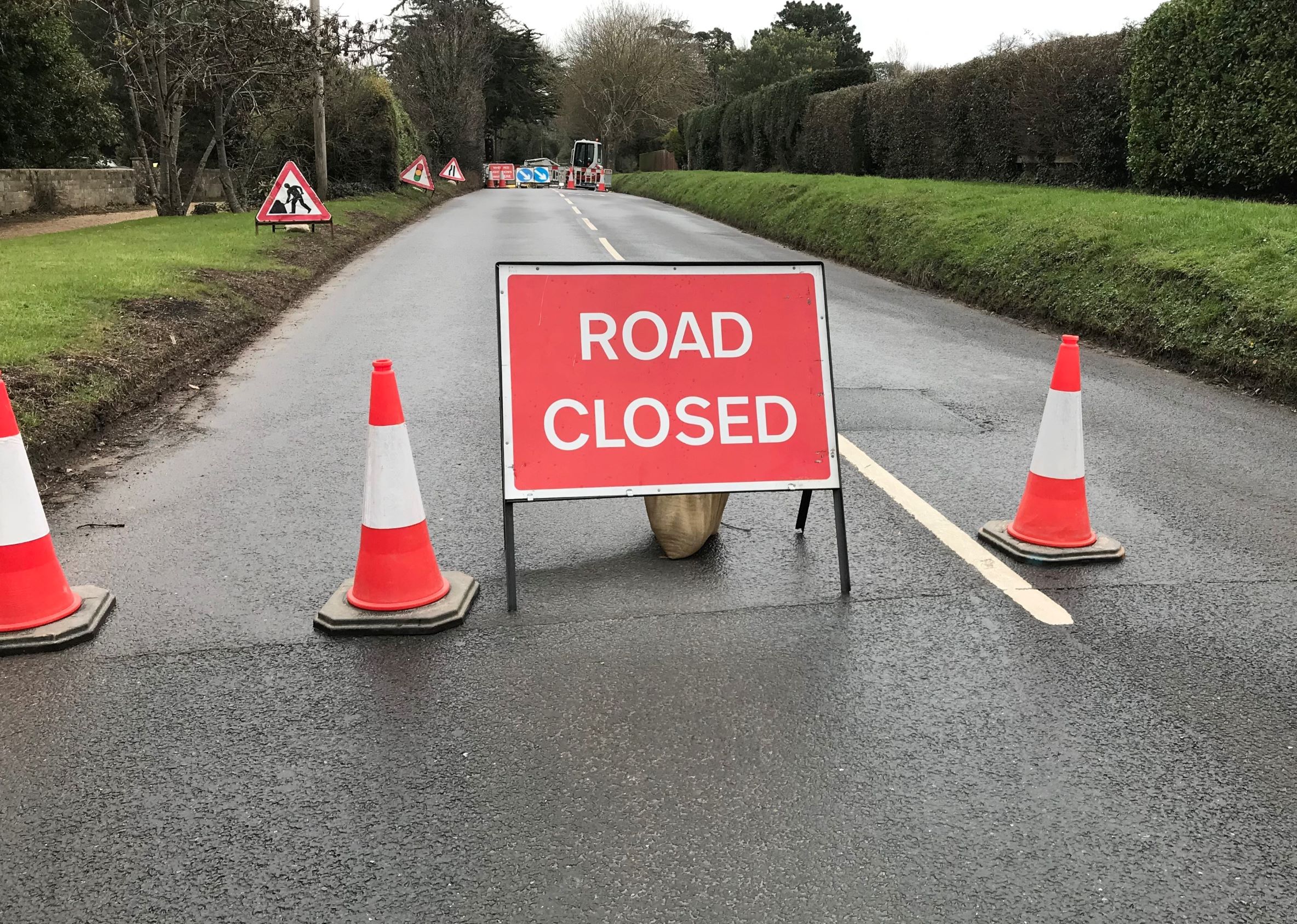 Photo showing road closed sign and traffic cones in the foreground and works equipment and machinery in the background in the middle of the road.