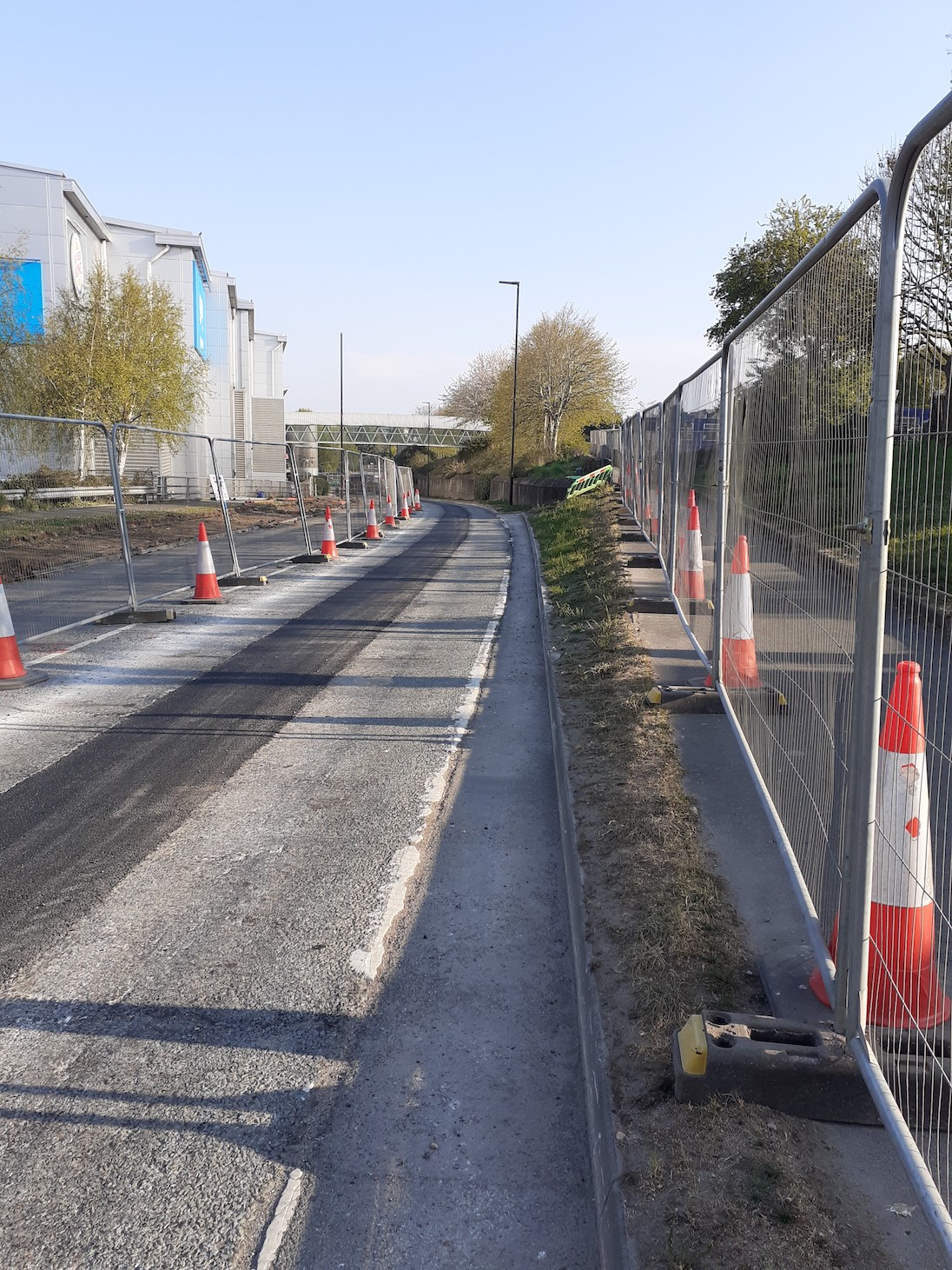 road with fencing on either side and traffic cones, surface of the road showing work underway