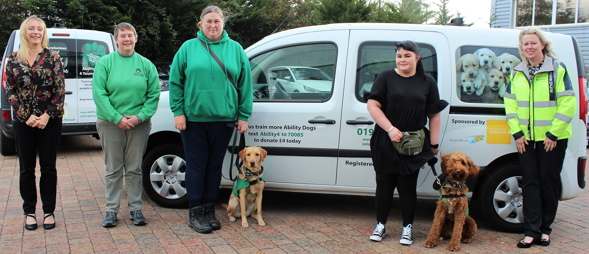 five people and two ability dogs standing in front of a vehicle