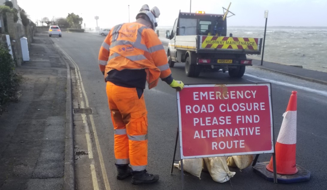 emergency road closure sign on road with island roads employee standing next to it