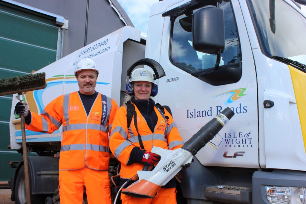 Two Island Roads staff in full gear with leaf cleaning equipment standing in front of a mechanical leaf sweeper ready to go into action.