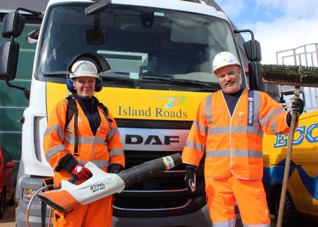Two Island Roads staff in full gear with leaf cleaning equipment standing in front of a mechanical leaf sweeper ready to go into action.