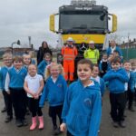 group of children standing in front of a gritting vehicle