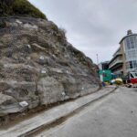 unsurfaced road with rock face to the left covered with netting. A work van can is parked at the end of the road