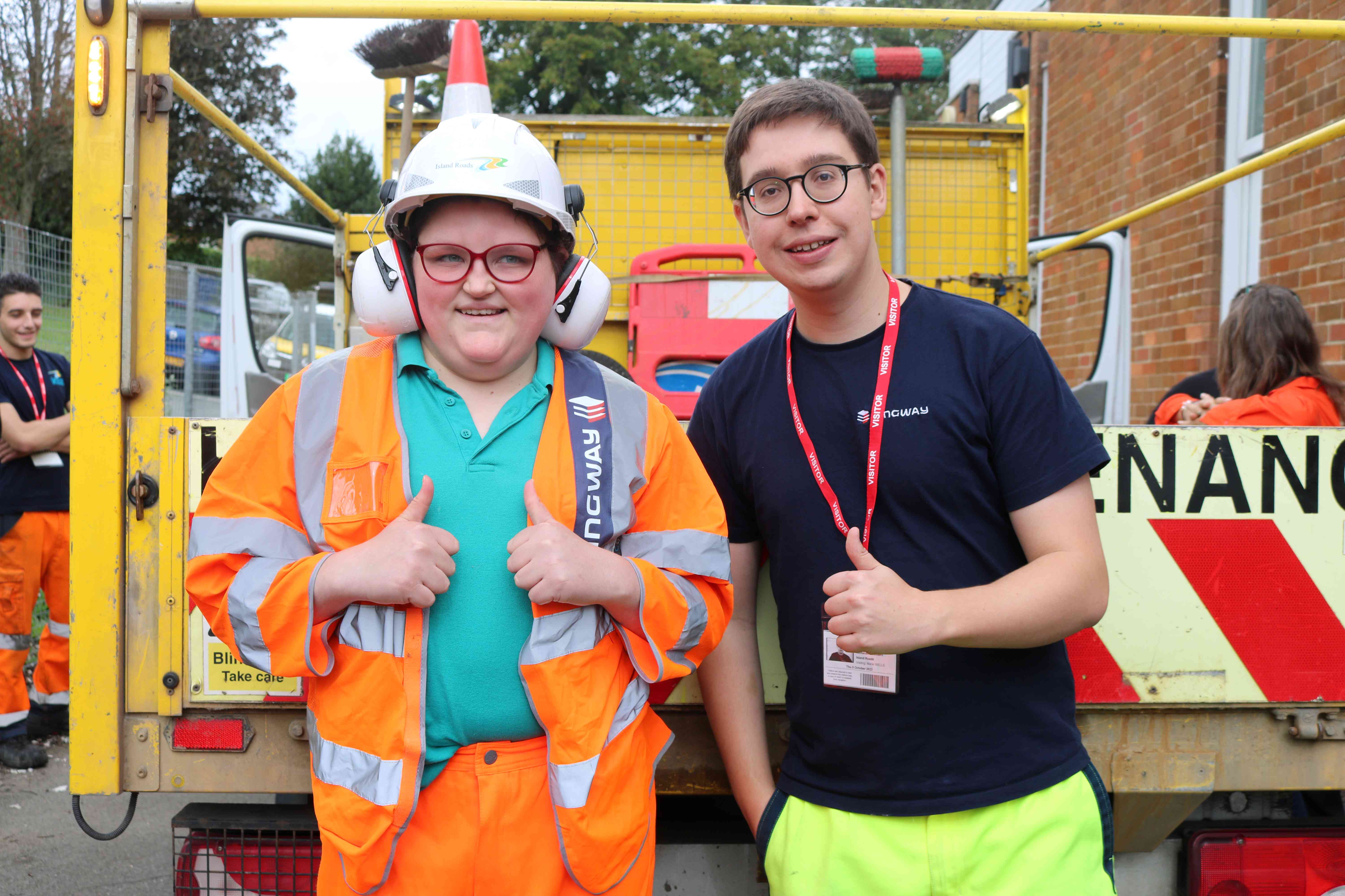 A member of Island Roads staff standing behind an Island Roads vehicle with a young person who is wearing Island Roads uniform as part of an educational session being run by Island Roads
