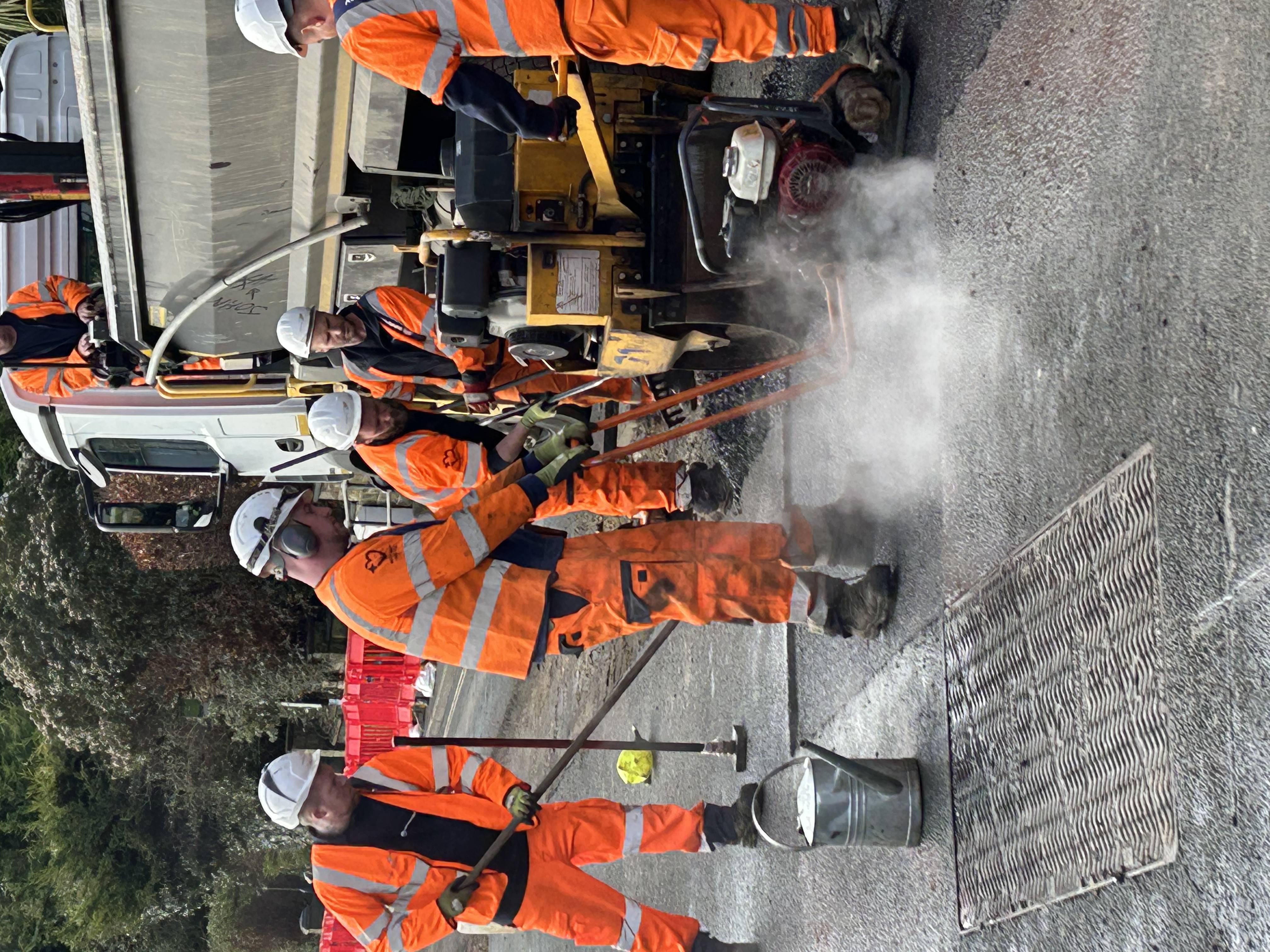 workmen in orange protective clothing resurfacing a road